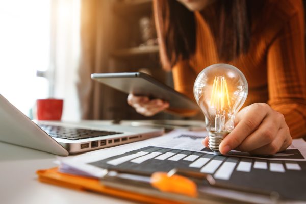 Business,Hand,Holding,Lightbulb,With,Using,Laptop,Computer,And,Money