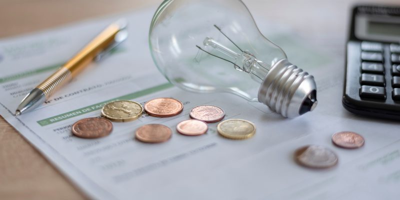 Electricity bill with light bulb, several coins, calculator and pen on the desk. Concept of electricity prices and tax payments.